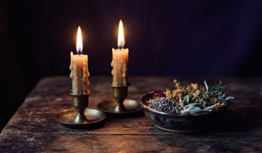Two lit candles beside a bowl of herbs, representing themes related to are love spells dangerous.